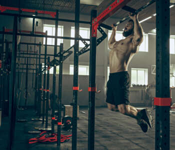 Concept: power, strength, healthy lifestyle, sport. Powerful attractive muscular man trainer do pull ups during workout at the gym